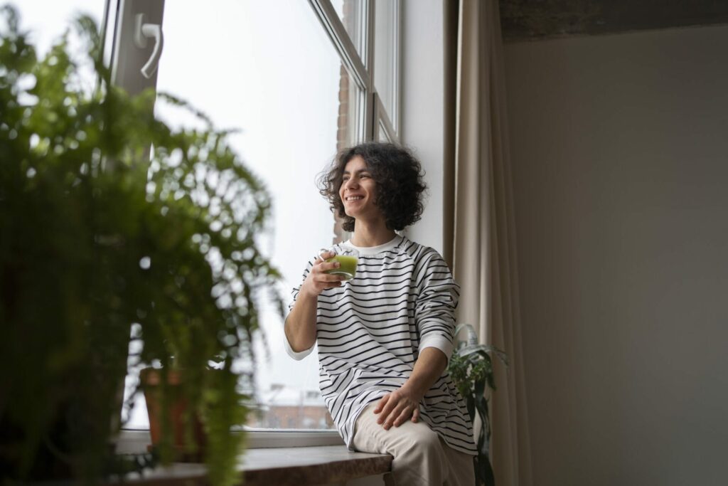 Person sitting in front of a window while drinking a beverage.